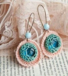 two crocheted earrings with blue beads on top of a piece of fabric next to lace