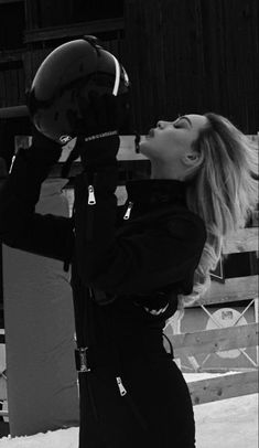 black and white photograph of a woman holding a helmet up to her face while standing in the snow