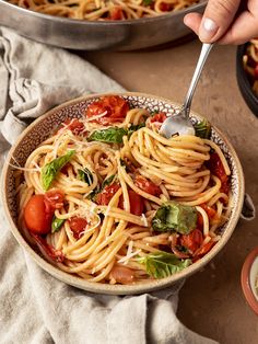 a bowl of pasta with tomatoes, basil and parmesan cheese being spooned into it