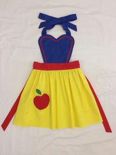 a yellow and blue dress with an apple on the front, red ribbon around the waist