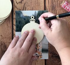 a person is holding a pen and writing on a card with an ornament