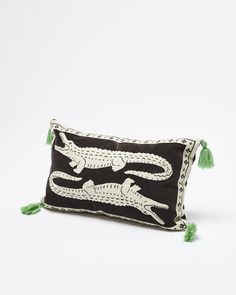 a black pillow with an alligator design on the front and green tassels around the edges