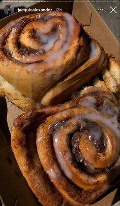 two cinnamon rolls in a box with icing on top and another one wrapped in brown paper