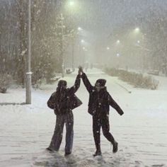 two people standing in the snow with their arms up and one person raising their hands