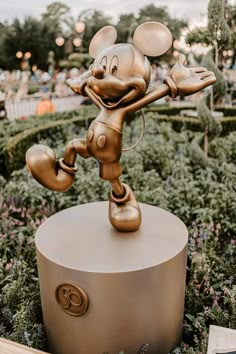 a bronze mickey mouse statue in the middle of a flower garden at disney world's animal kingdom