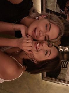 two beautiful young women standing next to each other in front of a mirror smiling at the camera