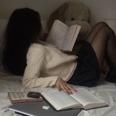 a woman laying in bed reading a book and holding an apple laptop next to her