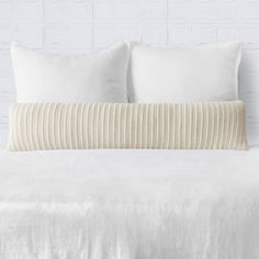 a bed with white sheets and pillows in front of a brick wall on the side