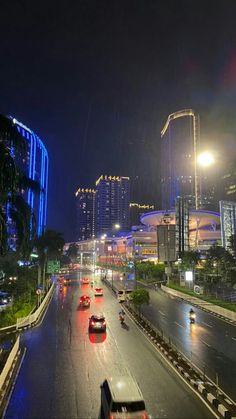 cars driving down the road at night in an urban area with tall buildings and skyscrapers