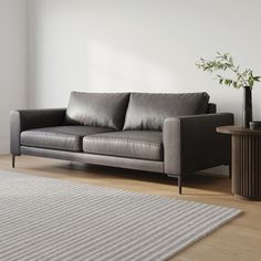 a gray couch sitting on top of a wooden floor next to a vase with a plant