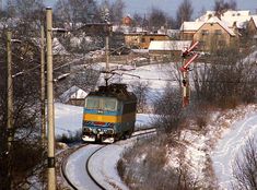 a train traveling down tracks next to snow covered trees and houses in the background with buildings on either side