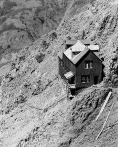 a black and white photo of a house on the side of a mountain