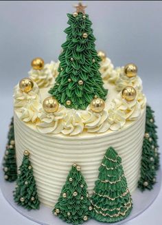 a christmas cake with white frosting and green trees on top, decorated with gold ornaments