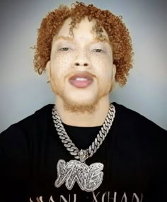 a young man with curly hair wearing a black t - shirt and silver chain necklace