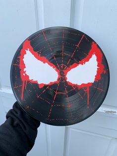 a hand holding up a black and red record with white wings on it's face