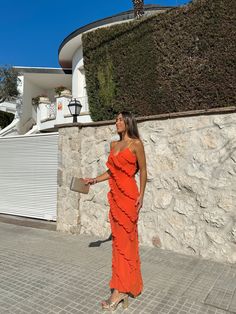 a woman in an orange dress is standing outside