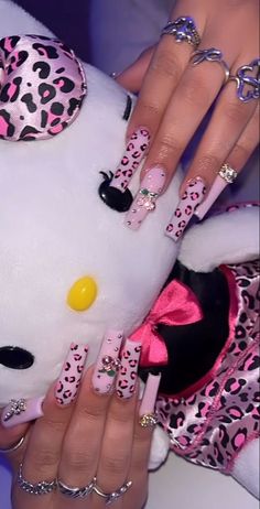 a woman with pink and black leopard print nails holding a white stuffed animal in her hand