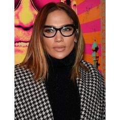 a woman wearing glasses and a black turtle neck sweater stands in front of a colorful background