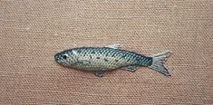 a small fish is sitting on a brown fabric surface, it appears to be needle - embroidered