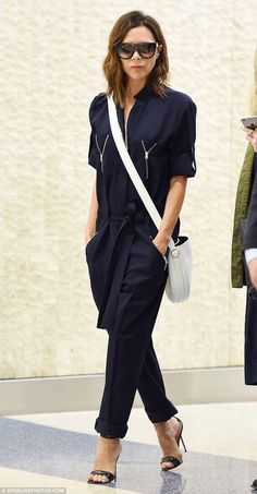 a woman in black jumpsuits and sunglasses walking through an airport