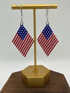 a pair of earrings with an american flag design on them sitting on a wooden stand