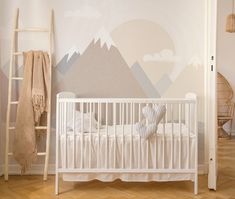 a white crib in front of a wall with mountains painted on it and a ladder leaning against the wall