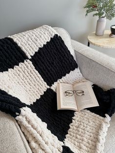 an open book is laying on top of a black and white crocheted blanket