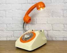 an orange and white telephone sitting on top of a wooden table next to a brick wall