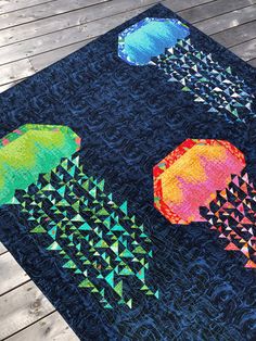 an umbrella quilt is displayed on a wooden deck in front of some trees and water