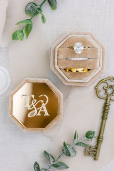 two wedding rings and an engagement ring box on top of a table with greenery