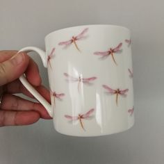 a hand holding a white coffee cup with pink dragonflies on the outside and inside