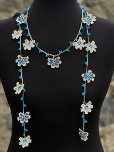 a woman wearing a necklace with blue and white flowers on the front, attached to a black mannequin