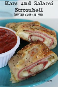 ham and salami stromboli on a blue plate with a bowl of tomato sauce