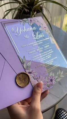 a person holding up a purple and silver wedding card with a wax seal on it