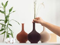 three vases are sitting on a table with one being held over the other by a person's hand