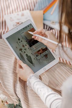 a woman sitting on a bed using an ipad with a pen and paper in her hand