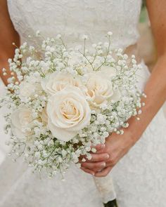 a bride holding a bouquet of white roses and baby's breath in her hands