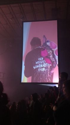 a man standing on top of a stage in front of a large screen with words