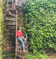 a woman sitting on top of a metal spiral staircase next to a lush green wall