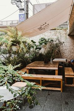 an outdoor dining area with wooden tables and benches under a tarp over the patio