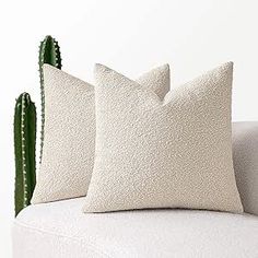 two pillows sitting on top of a white couch next to a green cactus in the corner