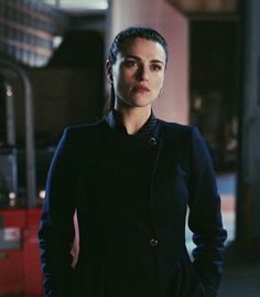 a woman standing in front of a red double decker bus wearing a black coat and jeans