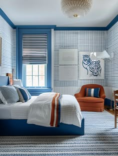 a bedroom with blue walls and white bedding, orange chair, and patterned rug