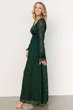 a woman wearing a green dress with sheer sleeves and long sleeves, standing in front of a