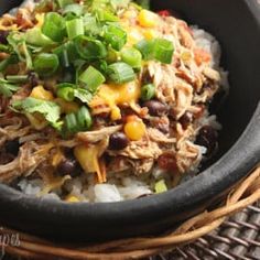 a black bowl filled with rice, beans and shredded meat topped with green onions on top