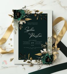 an elegant wedding card with gold and green flowers on it, next to a black ribbon