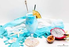 a blue drink in a glass next to some fruit on a white tablecloth with an umbrella