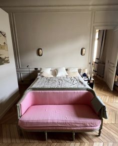 a pink couch sitting in front of a white bed on top of a hard wood floor