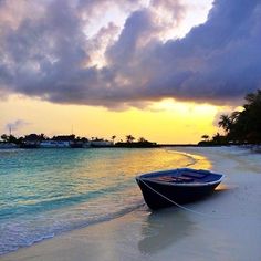 a boat is sitting on the beach in front of some water and clouds at sunset