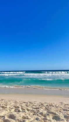 an empty beach with waves coming in to the shore and a blue sky above it